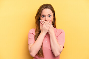 Young caucasian woman isolated on yellow background shocked covering mouth with hands.