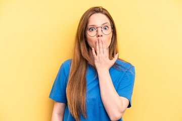 Young caucasian woman isolated on yellow background shocked, covering mouth with hands, anxious to discover something new.