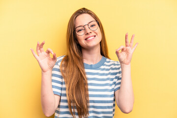 Young caucasian woman isolated on yellow background cheerful and confident showing ok gesture.
