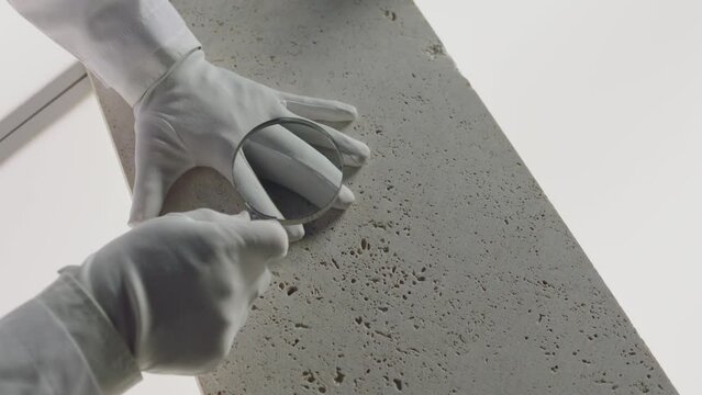 Construction laboratory testing the quality density of natural travertine stone . Worker of laboratory explore stone by loupe . Close up view of hands with gloves . Shot on ARRI Alexa cinema camera