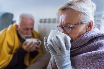 Couple covered with blanket drinking tea beside radiator