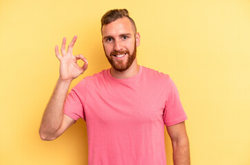 Young caucasian man isolated on yellow background cheerful and confident showing ok gesture.