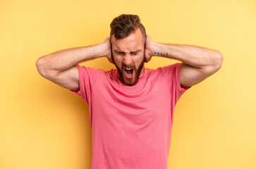 Obraz premium Young caucasian man isolated on yellow background covering ears with hands trying not to hear too loud sound.