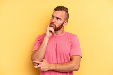 Young caucasian man isolated on yellow background thinking and looking up, being reflective, contemplating, having a fantasy.