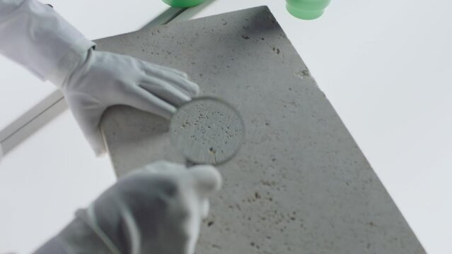 Construction laboratory testing the quality density of natural travertine stone . Worker of laboratory explore stone by loupe . Close up view of hands with gloves . Shot on ARRI Alexa cinema camera