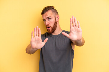 Young caucasian man isolated on yellow background standing with outstretched hand showing stop...