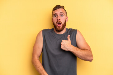 Young caucasian man isolated on yellow background surprised pointing with finger, smiling broadly.