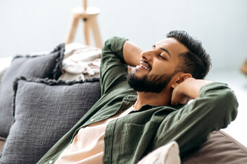 Satisfied calm arabian or indian attractive young man relaxing on the sofa at home in the living...