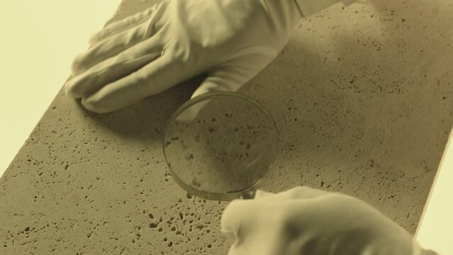 Construction laboratory testing the quality density of natural travertine stone . Worker of laboratory explore stone by loupe . Close up view of hands with gloves . Shot on ARRI Alexa cinema camera