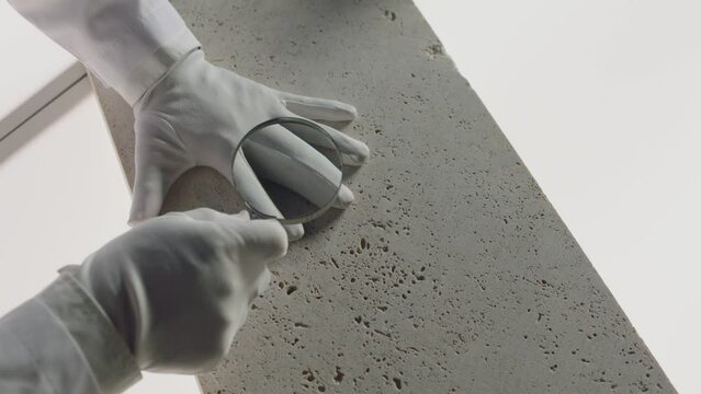 Construction laboratory testing the quality density of natural travertine stone . Worker of laboratory explore stone by loupe . Close up view of hands with gloves . Shot on ARRI Alexa cinema camera