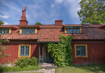 Fototapeta na wymiar Old wood 1800s red house with dorms, tin chimney and entrance covered in flower leaves, a summer day in Stockholm