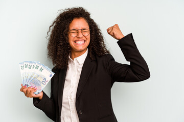 Young business Brazilian woman holding banknotes isolated on white background raising fist after a...