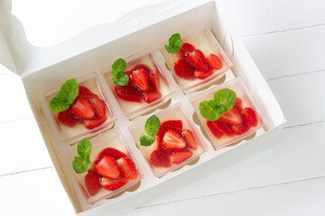 Strawberry panna cotta in a jelly, portion cups in delivery box. Strawberry jelly