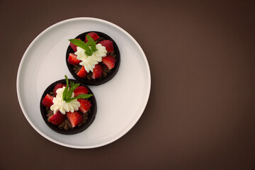 Mini chocolate tarts with fresh strawberries, wiped cream and mint leaves. Strawberry tarts