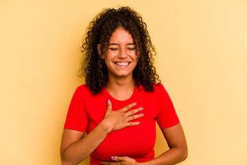 Young Brazilian woman isolated on yellow background laughs happily and has fun keeping hands on...