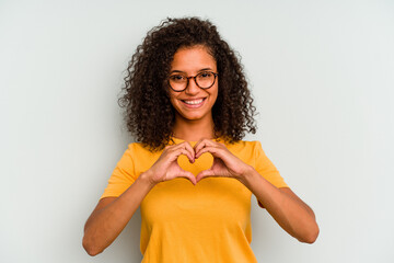 Young Brazilian woman isolated on blue background smiling and showing a heart shape with hands.