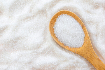 Fototapeta na wymiar White granulated sugar and a wooden spoon in sugar. Top view