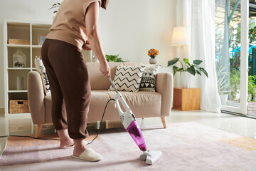 Close-up of housewife using vacuum cleaner to vacuum the carpet in living room during housework at...