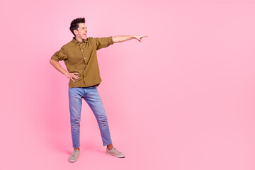 Full length photo of smiling young man pointing fingers empty space aside in isolated studio light pastel background