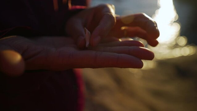 A woman's hand holds out an animal tooth found outside near the water during a golden hour sunset, flips the tooth over. Close up.