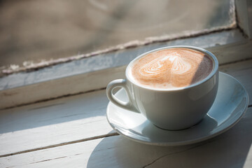 Cappuccino with cinnamon in a white cup on window sill