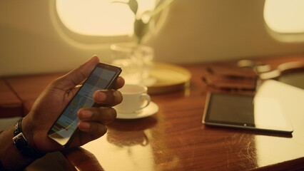 Businessman using cell phone on flight. Closeup hands hold smartphone in plane