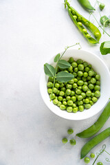Green fresh peas, snack pea in a white bowl on a neutral grey background. Top view. Summer garden vegetables.