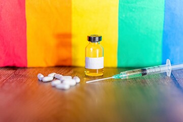 Syringe, vaccine vial and medicinal tablets in the background of a pride rainbow flag