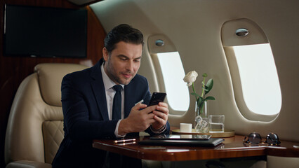 European businessman typing phone on airplane trip. Confident manager resting