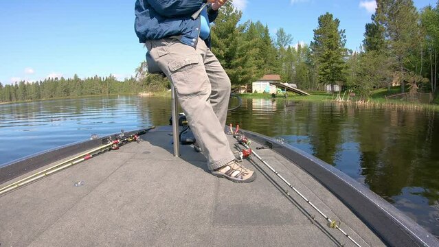 Man fishing with an open face reel and artificial lure while leaning on a butt seat in the front of a bass boat; near docks on Lake Vermilion on a sunny spring day; concepts of fishing and vacation