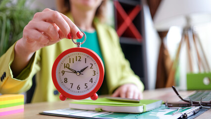 Businesswoman holding alarm clock in hand, time management and deadline