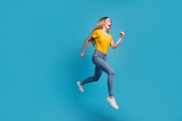 Fototapeta na wymiar Portrait of sportive active girl in motion jumping over in the air isolated on blue background having perfect stretching