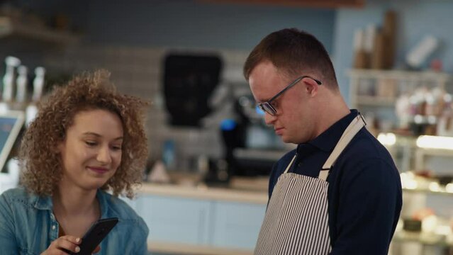 Caucasian waiter with down syndrome accepting contactless payment in the cafe from the client. Shot with RED helium camera in 8K.  