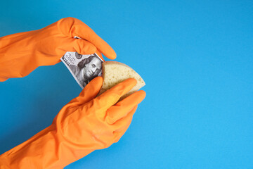 hands in orange gloves wash money with soap and sponge on a blue background