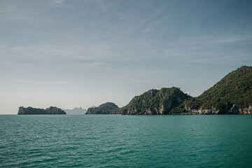 Fototapeta premium Don Sak, Nakhon Si Tammarat, Thailand - December 23rd, 2019 : views from a boat of the sea shore in Donsak, Nakhon SI Tammarat on a sunny day with limestone cliffs in the background