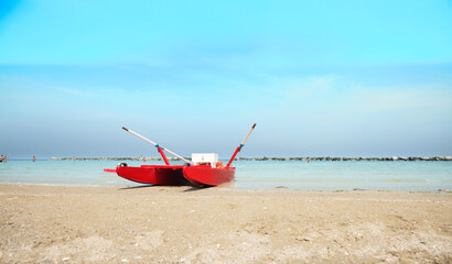 Lifeboat with lifebuoy and oars on the beach in a sunny summer day, in the background the Adriatic sea, Italy.