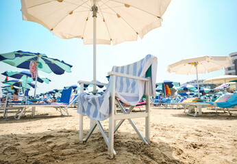 Chair with striped towel under an umbrella le at the beach on a sunny summer day. In the...