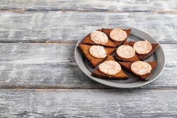 Sausage and toast on a gray plate on a gray wooden background. Side view, copy space.