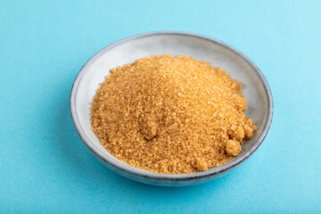plate with unrefined golden cane sugar on blue pastel. side view, close up.