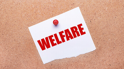 White paper with the text WELFARE is attached to the wooden background with a red button.