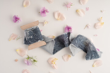 gray velvet ribbon on white background with flower petals next to it, top view. Decor for the wedding