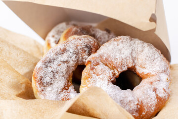 Fresh doughnuts sprinkled with powdered sugar on kraft napkins in a cardboard box. Donuts close-up....