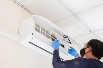 The technician wear face mask and face shield, A Hand of technician Man is cleaning on air conditioner after their use. Cleaning to prevent the virus and dust , maintenance air conditioner.