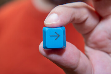 Close-up of a man's hand with a button from the keyboard. Blue plastic button with right arrow