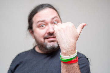 An unshaven man with bracelets in the colors of the Bulgarian flag gestures with his thumb to the side. Selective focus on the bracelet.