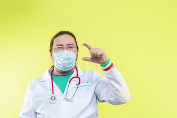 A doctor in a white coat and mask shows a small size with his fingers. Bracelet in the colors of the flag of Italy.
