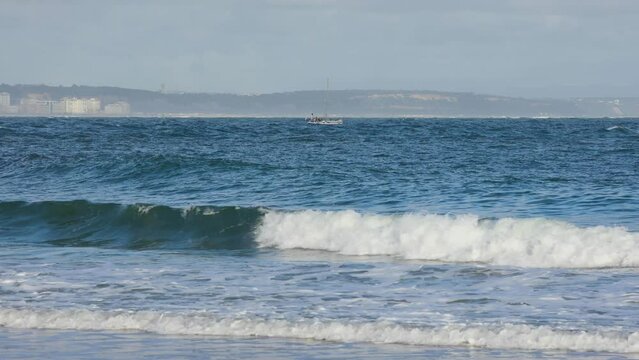 small boat moving in front of Costa da Caparica near Lighthouse of Torre do Bugio. Lisbon Guide Light. View from Fort S&atilde;o Juli&atilde;o da Barra Lighthouse.