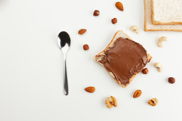 Square bread for toast with chocolate spread. Nuts, spoon, slices of bread and a sandwich with chocolate spread on a white table.