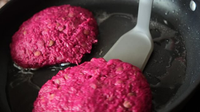 Vegan beetroot lentil burger cutlet frying in black frying pan. Cooking healthy food.