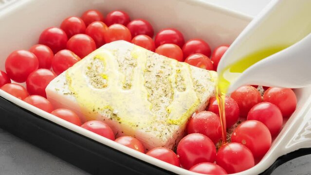 Baked feta cheese with tomatoes in dish. Pouring oil on feta and tomato. Trendy homemade recipe.